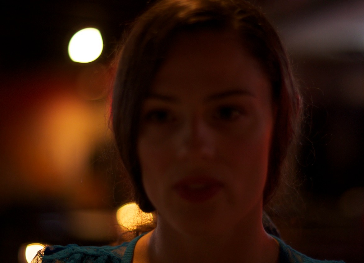 We are in a dark restaurant at night. It is all mood lighting. Candles on the tables, a small fixture by the entrance, and some light coming in behind the model on the right from the bar. This is what we get without any external lighting. [ No lights. Pentax K5, Revuenon 55mm f/1.2, 1/15s, ISO 800 ]